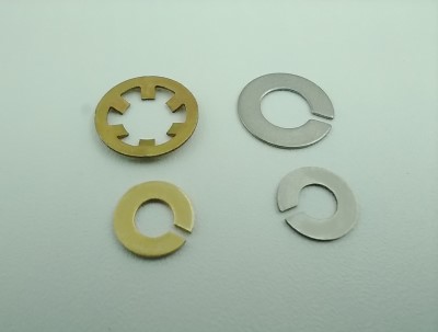 Four retaining rings are displayed on a light surface. The rings vary in design and color, with two being gold and two silver. Each has a unique shape, including slotted and circular styles.
