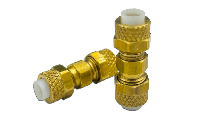 Two brass union fittings with textured grip surfaces and white inner components are shown. One fitting is upright, while the other is lying on its side.