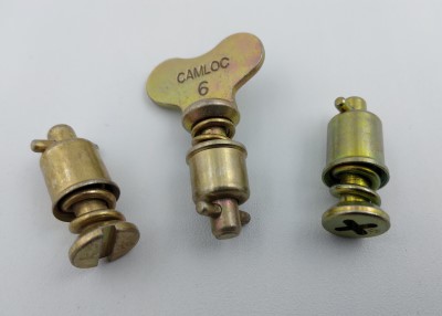 Three metal fasteners from the 4002 Series Camloc Stud collection are displayed. The central piece has a butterfly-shaped head labeled "CAMLOC 6," flanked by two cylindrical fasteners with different slot designs.