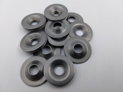 A pile of 601 Finishing Washers with an 82° angle, featuring a smooth, metallic finish and a central hole. The washers are arranged on a light gray surface.