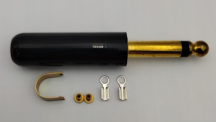 The image shows a gold and black headset plug with accompanying components, including a U-shaped clip, two small gold rings, and two metallic connectors, arranged on a light surface.