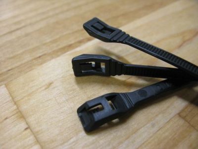 Three black 14" low profile cable ties on a wooden surface, showing their locking mechanisms.