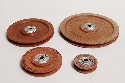Four phenolic cable pulleys of varying sizes are displayed on a white background. The pulleys have a textured brown surface and silver centers, showcasing their design and material.