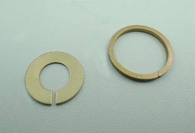 Two metal rings on a light surface; the left is a retaining ring with a gap, and the right is a snap ring, both used for securing components in machinery.