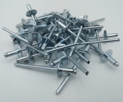 A pile of silver pop rivets with flange heads scattered on a white surface.