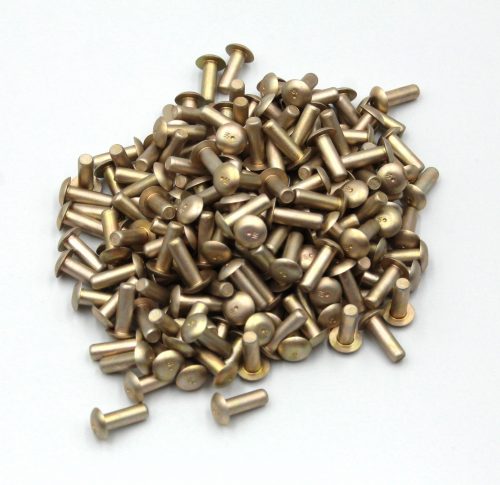 A pile of MS20470 Universal Head Solid Rivets in a metallic finish, scattered on a white surface.