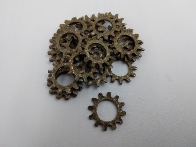 A pile of metal split lock washers on a white surface, with one washer separated in the foreground. The washers have a toothed, gear-like appearance.