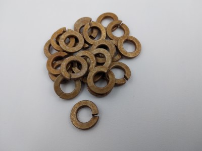 A pile of bronze split lock washers on a white surface. The washers are circular with a cut that creates a slight gap, designed to prevent loosening of fasteners.