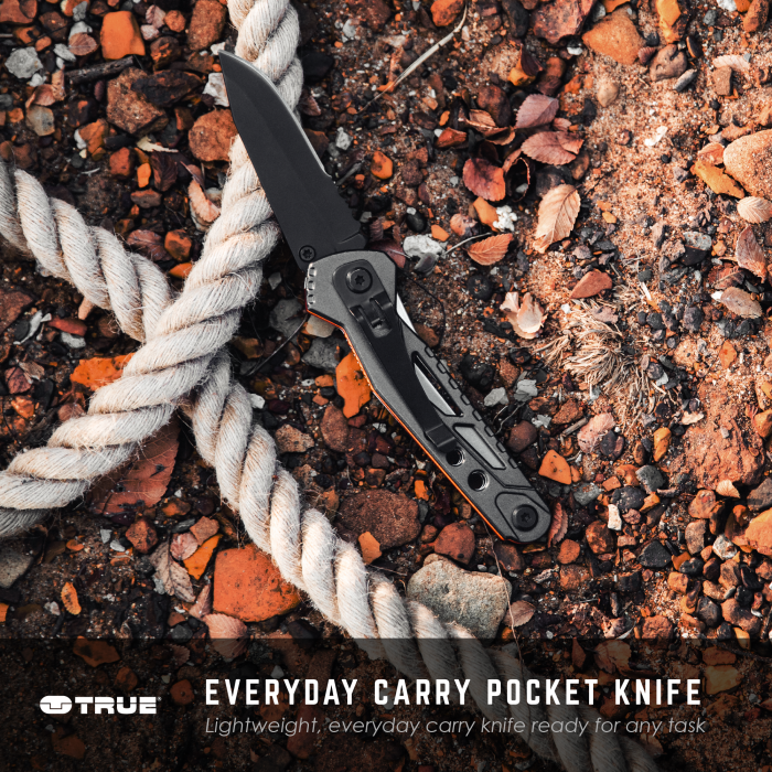 A "Trueblade" everyday carry pocket knife with a black blade and handle is open on a ground covered with rocks and coiled rope. The knife is designed for lightweight, versatile use.
