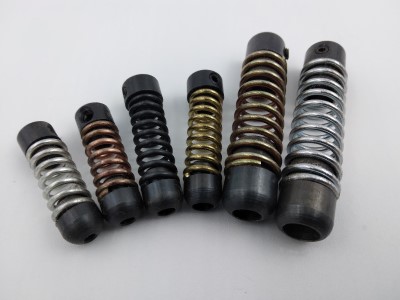 Six drill stops of varying sizes arranged in a row, each featuring a coiled spring design with different metal finishes, including silver, black, and gold, against a plain white background.