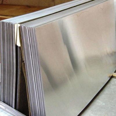 Stack of large, shiny metal sheets leaning against a wall on a concrete floor.