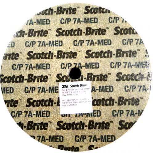 A round Scotch-Brite 6" wheel with a textured surface, featuring the brand name and model details printed repeatedly in black text on a beige background.