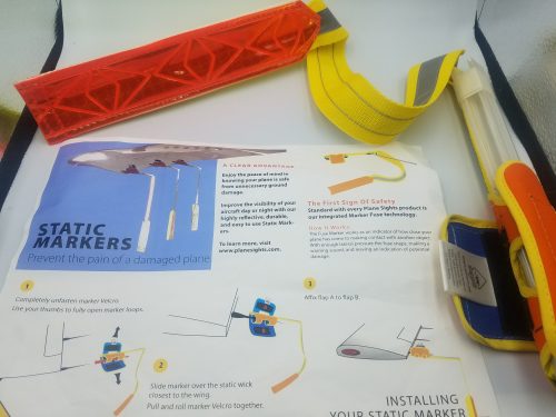 Instruction sheet for "STATIC WING MARKER" with diagrams and text on installation. A red and yellow tool is partially visible on the right, with a yellow strap attached.
