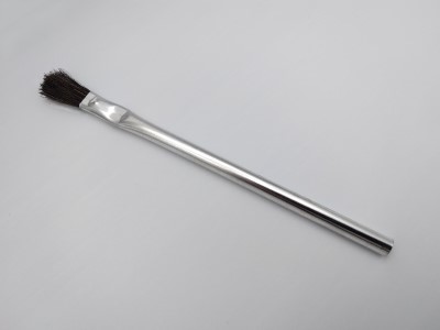 A metal tubular brush with a long, shiny handle and dark bristles, placed diagonally on a light gray background.