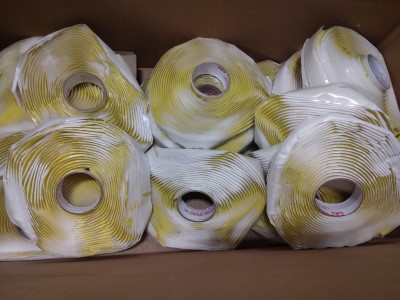 Rolls of yellow and white sealant tape with visible damage are stacked in a cardboard box.
