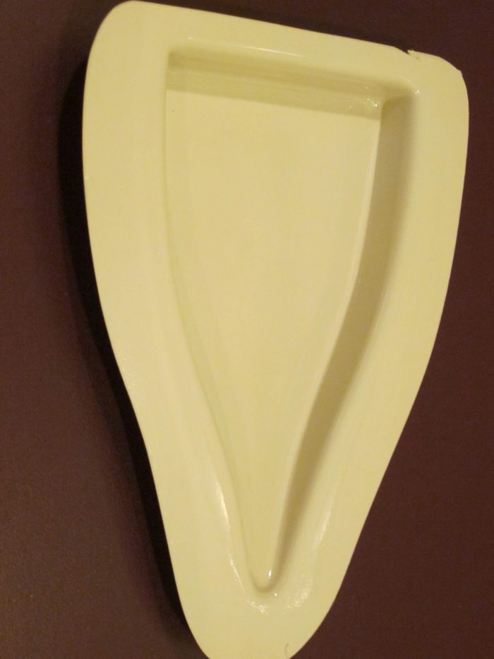 Cream-colored, wall-mounted urinal with a smooth, elongated shape against a dark brown wall.