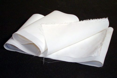 A piece of white, folded paper with frayed edges lies on a dark surface.