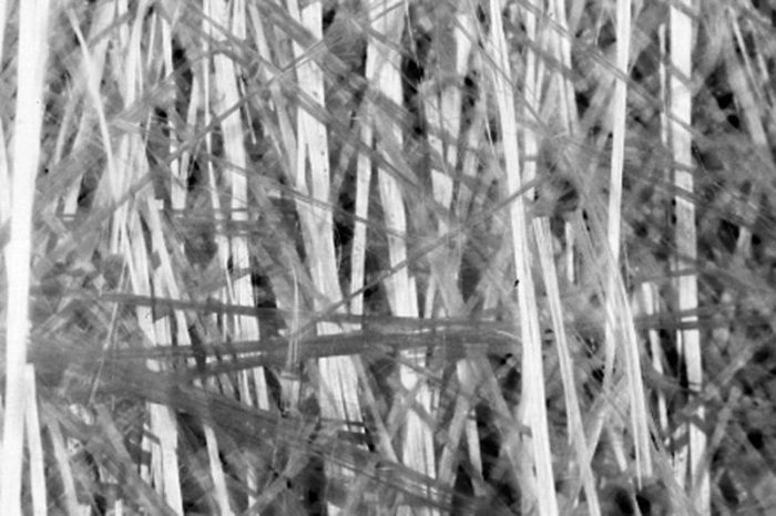 Close-up of tangled, overlapping strands of white and gray fibers, creating a dense, abstract pattern. The fibers vary in thickness and direction, forming a textured, chaotic appearance.