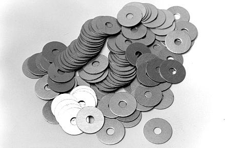 A pile of metal washers scattered on a surface. Most washers are dark, with a few lighter ones mixed in.