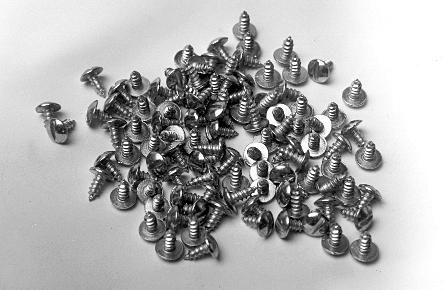 A pile of assorted metal screws on a white surface, including various sizes and head types.
