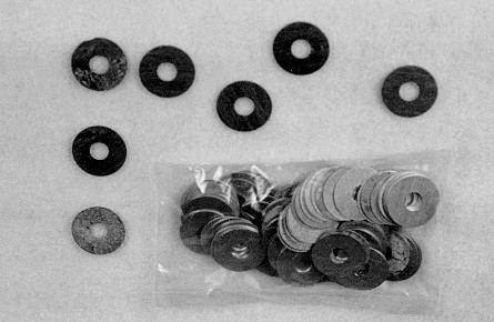 A collection of metal washers, with some arranged in a line above and others in a clear plastic bag below, against a plain background.