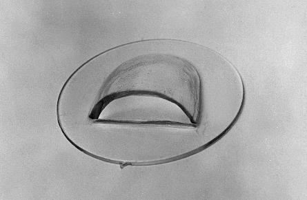 A black and white image of a metallic, dome-shaped UFO with a flat, circular base, hovering in a cloudy sky.