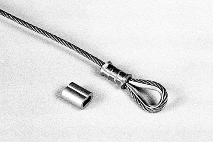 A steel wire rope with a looped end secured by a metal sleeve, next to a separate metal sleeve on a white background.