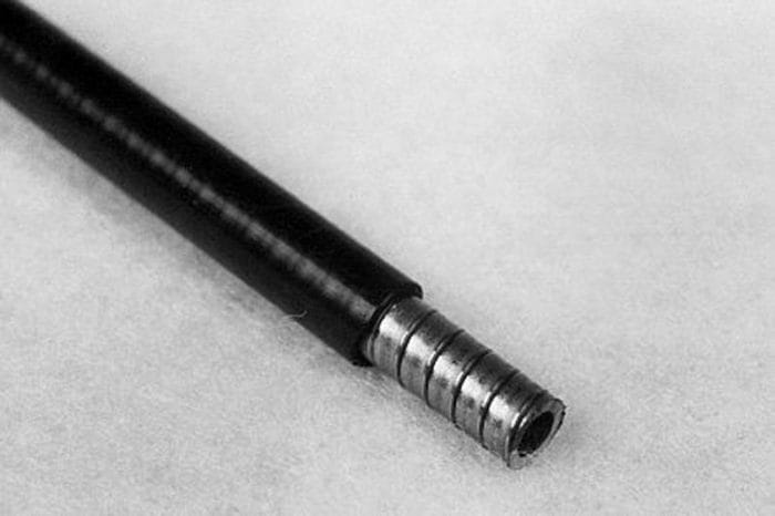 Close-up of a black cable with a metallic connector end, lying on a light gray surface.