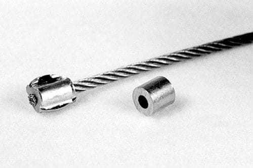 A metal cable with a cylindrical fitting attached on one end and a separate cylindrical piece nearby, both on a plain white background.