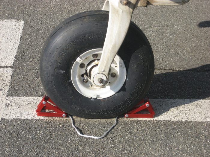 Airplane wheel secured with a red chock on an asphalt surface.