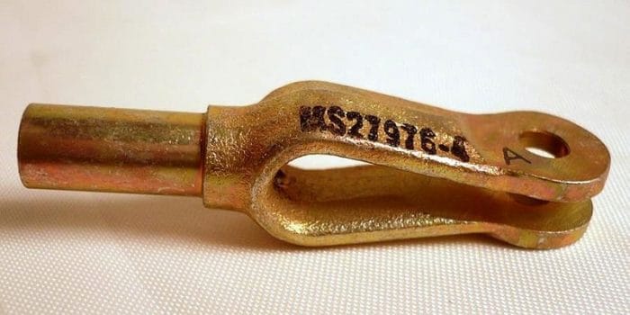 A metal clevis with a cylindrical end and a U-shaped fork, featuring a hole for a pin. It is marked with the code "MS21976-1" on the side. The clevis is placed on a light surface.