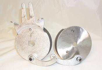 Two metal circular objects with a flat base, featuring a hand-like extension on the left one. They are connected by a curved metal strip. The background is a plain, light-colored surface.