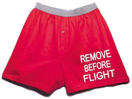 Red boxer shorts with a gray waistband and the phrase "REMOVE BEFORE FLIGHT" printed in white on the right leg.