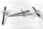 Three metal rivets with wide, flat heads and cylindrical shafts are arranged on a white surface. The rivets are positioned at different angles, showcasing their structure.