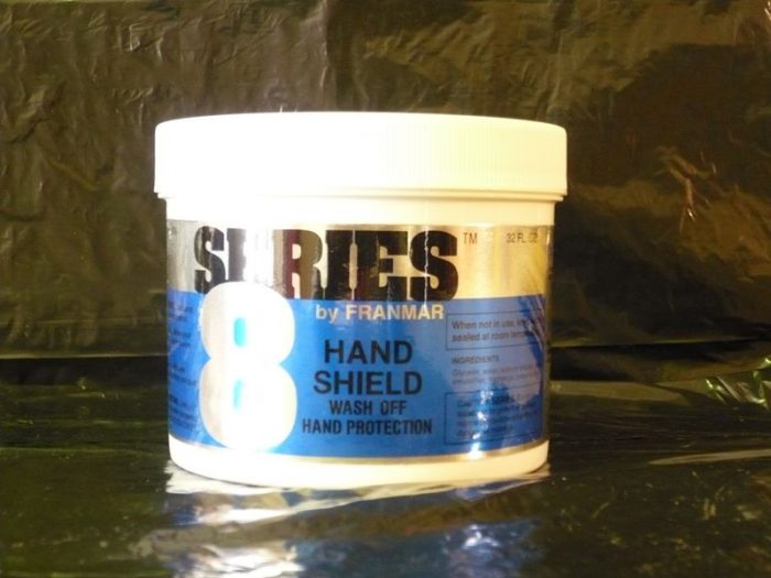 White container of Series 8 Hand Shield by Franmar, featuring a blue label with text indicating it is a wash-off hand protection product. The background is a dark, reflective surface.