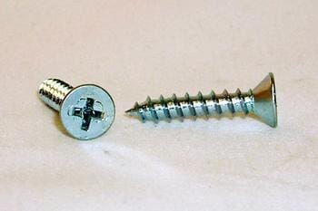 Two metal screws on a light surface; one is flat-headed with a cross-shaped groove and the other is a longer, pointed screw with the same type of groove.