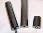 Three cylindrical carbon fiber tubes of varying heights are standing upright on a white surface. The tallest tube has a metal rod protruding from its base.