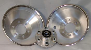 Two shiny metal brake drums are positioned upright, with a wheel hub assembly placed in front of them. The background is a plain white surface.