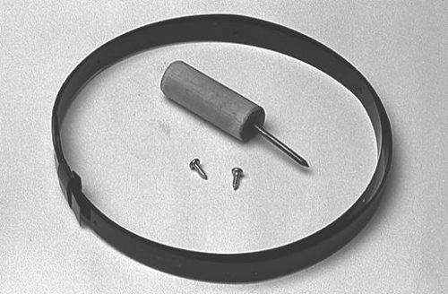 A black circular band, a metal punch tool with a wooden handle, and two small screws are arranged on a light gray surface.