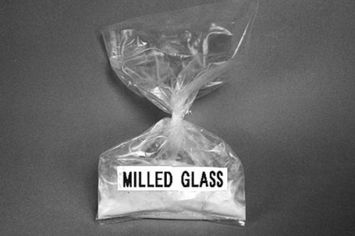 A clear plastic bag filled with fine white powder labeled "Milled Glass" against a gray background.