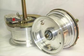 Two shiny metal reel components, one upright and the other lying on its side. The upright reel has a brass rod and a small red button. Both reels have a smooth, polished finish, set against a plain white background.