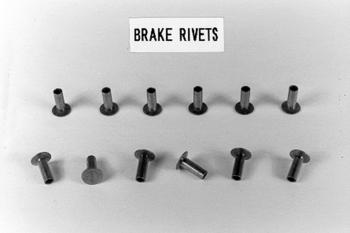 Twelve brake rivets arranged in two rows on a flat surface with a label above reading "Brake Rivets."