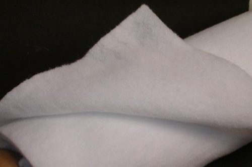 Close-up of a soft, white fabric with a slightly fuzzy texture, folded over itself against a dark background.