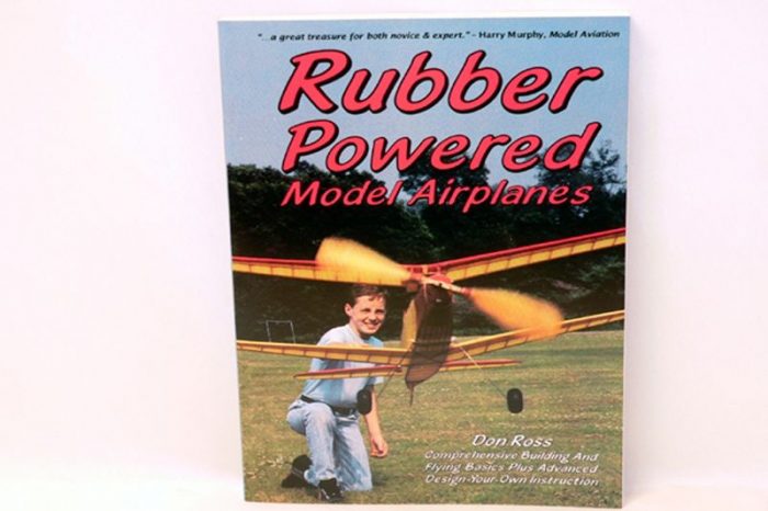 Cover of the book "Rubber Powered Model Airplanes" by Don Ross, featuring a child launching a model airplane in a grassy field. The title is in bold red letters, with a blue sky and trees in the background.