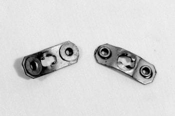 Two small, rectangular metal plates with circular and oval holes, placed on a plain surface.