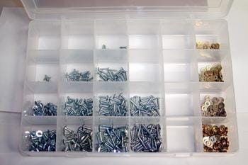 A plastic organizer box with multiple compartments, each containing various sizes and types of metal screws and fasteners. The screws are mostly silver, while some fasteners are brass-colored.
