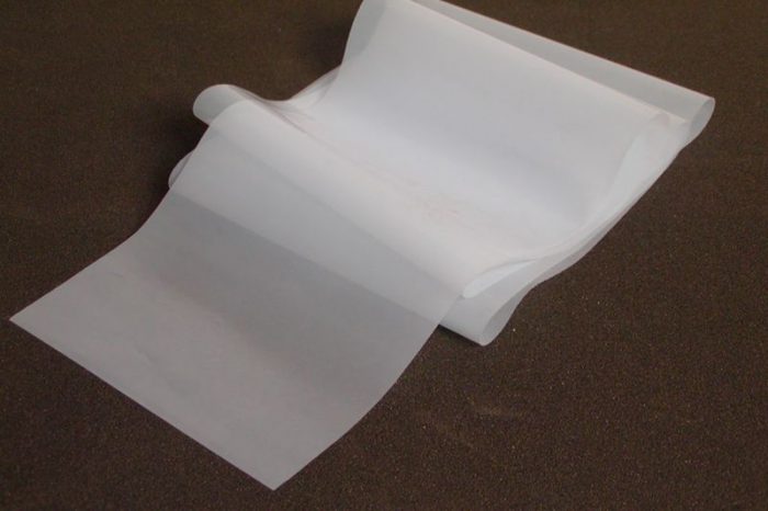 A large, white sheet of paper partially unrolled on a dark brown surface, creating gentle curves and folds.