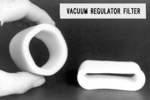 A hand holds a cylindrical foam filter next to a rectangular foam filter lying on a surface. A label above reads "Vacuum Regulator Filter."