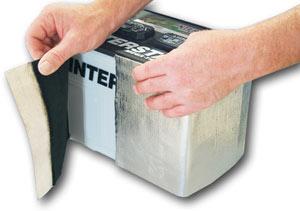 Hands applying a silver insulating wrap to a car battery, showing the process of covering the sides for thermal protection.