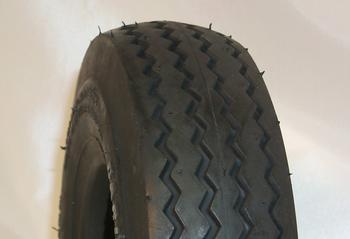 A black tire with a zigzag tread pattern is positioned upright against a plain white background.